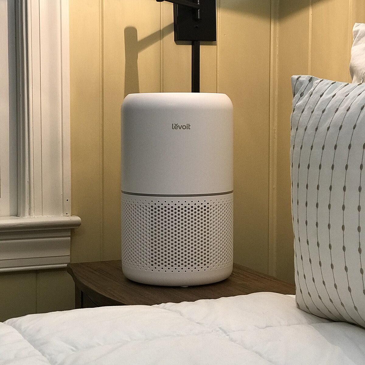 A Levoit Core 300-P air purifier on a nightstand next to a bed.
“Air Purifier (Levoit Core 300) (49318249796)” by Home Air Quality Guides is licensed under CC BY-SA 2.0.